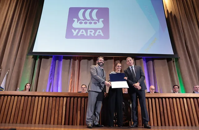 Pessoas sobre palco com telão com logo da Yara ao fundo